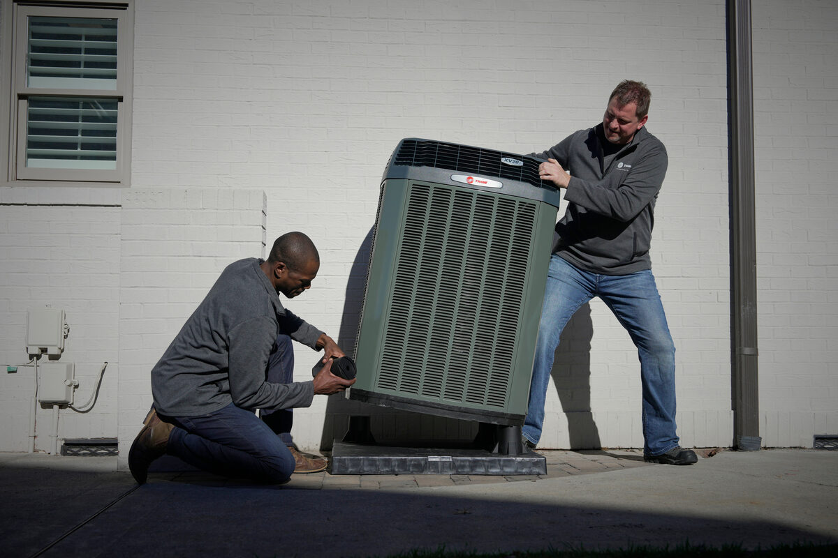 Two HVAC technicians working on an outdoor AC unit